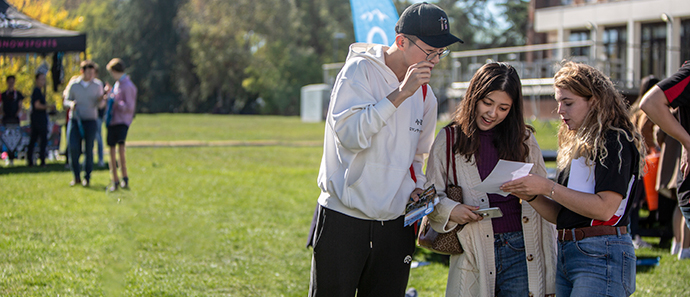 Three students look over a piece of paper intently while standing in the sunshine behind RUSU.