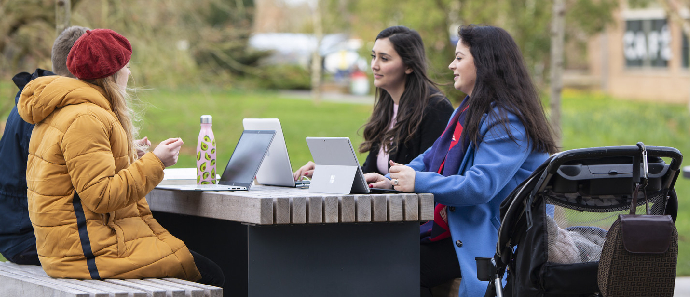 A group of women and a baby sat at a table with their laptops and tablets out.